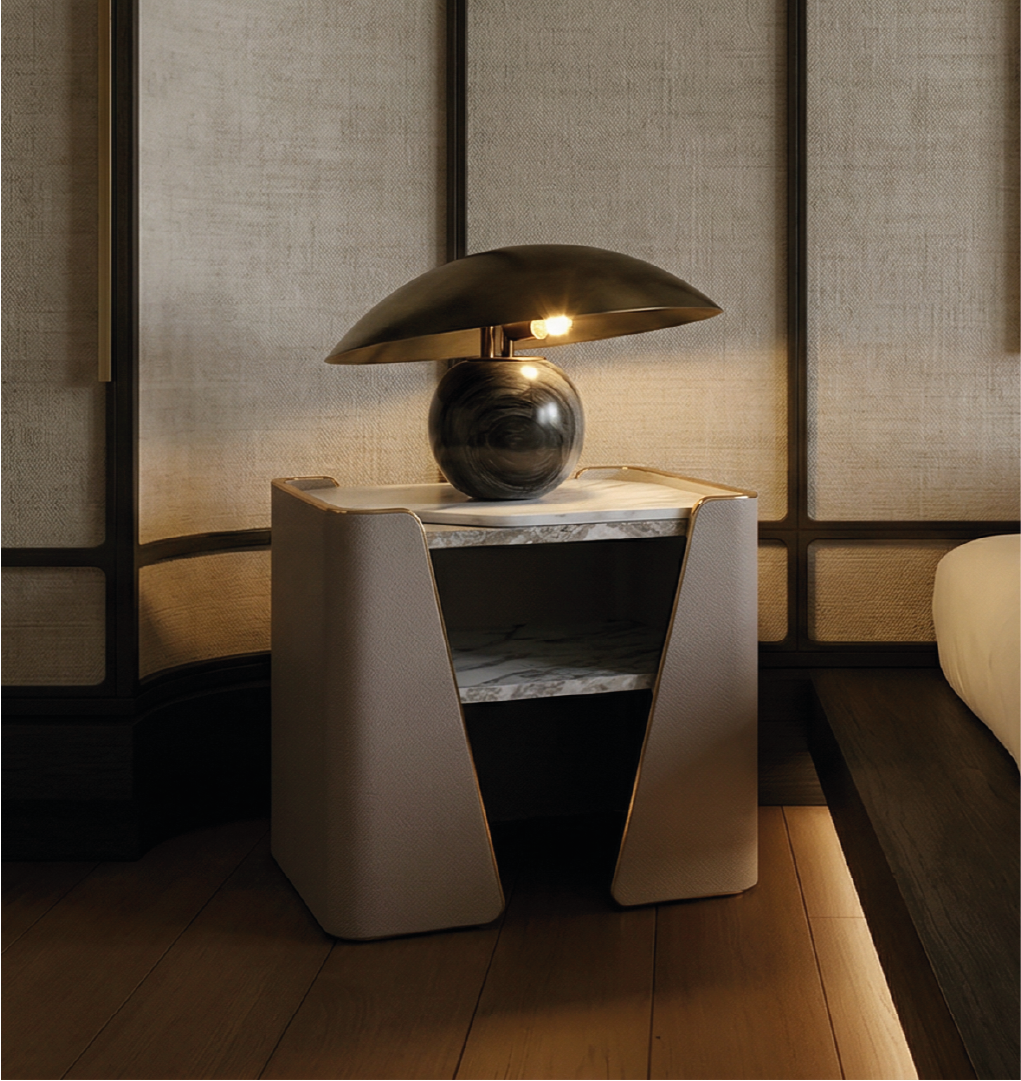 The Tallis Nightstand is a contemporary bedside piece that blends architectural design with luxurious materials. Featuring a sleek marble top, the nightstand is framed by softly curved, leather-wrapped sides that create a distinctive sculptural silhouette. An open shelf beneath the top provides practical storage while maintaining a light and airy visual profile. The combination of stone, leather, and metal accents reflects a refined modern aesthetic, making it ideal for upscale bedrooms or sophisticated interior settings. Both functional and visually striking, the Tallis Nightstand adds depth, texture, and elegance to any space.